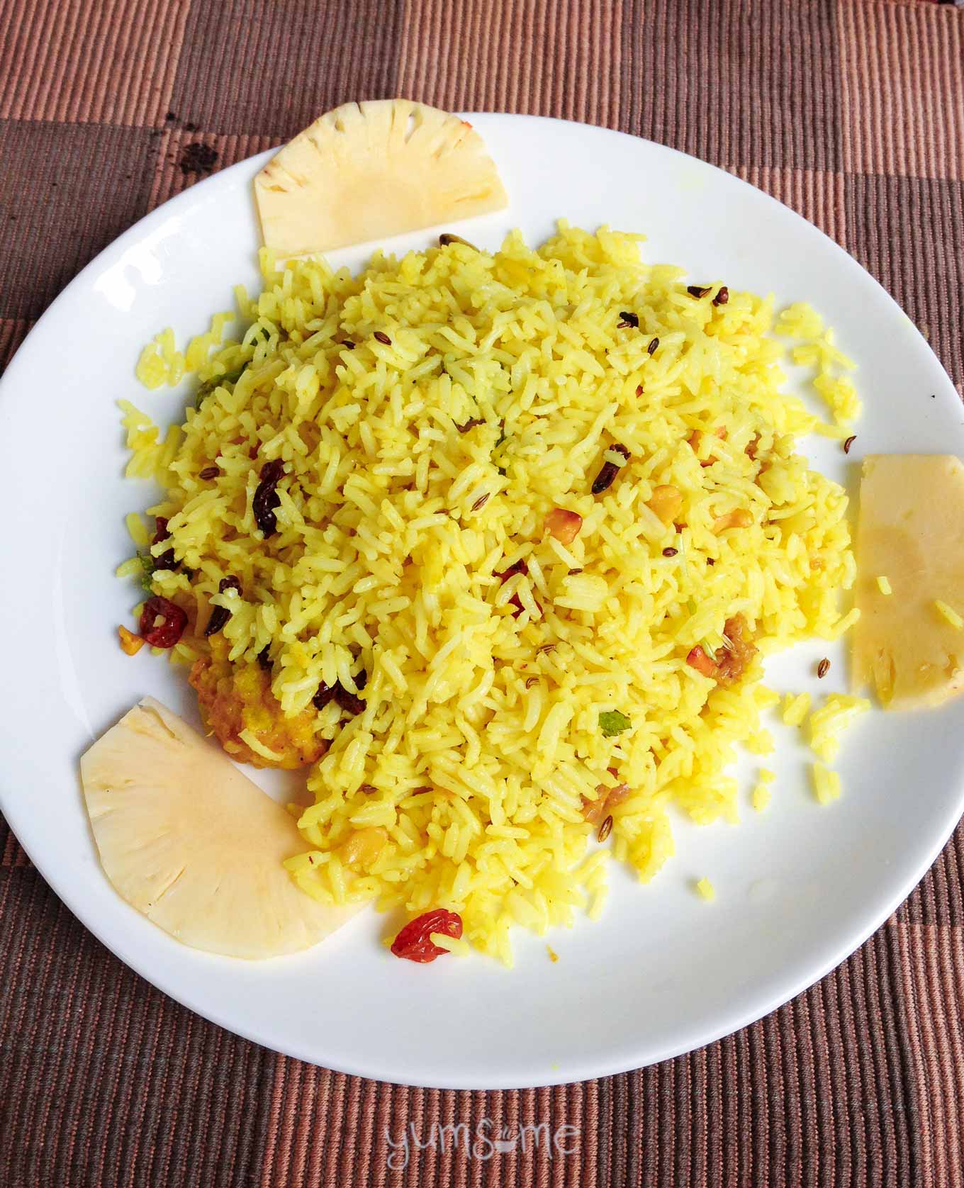 A white plate of vegetable biryani on a coloured background.