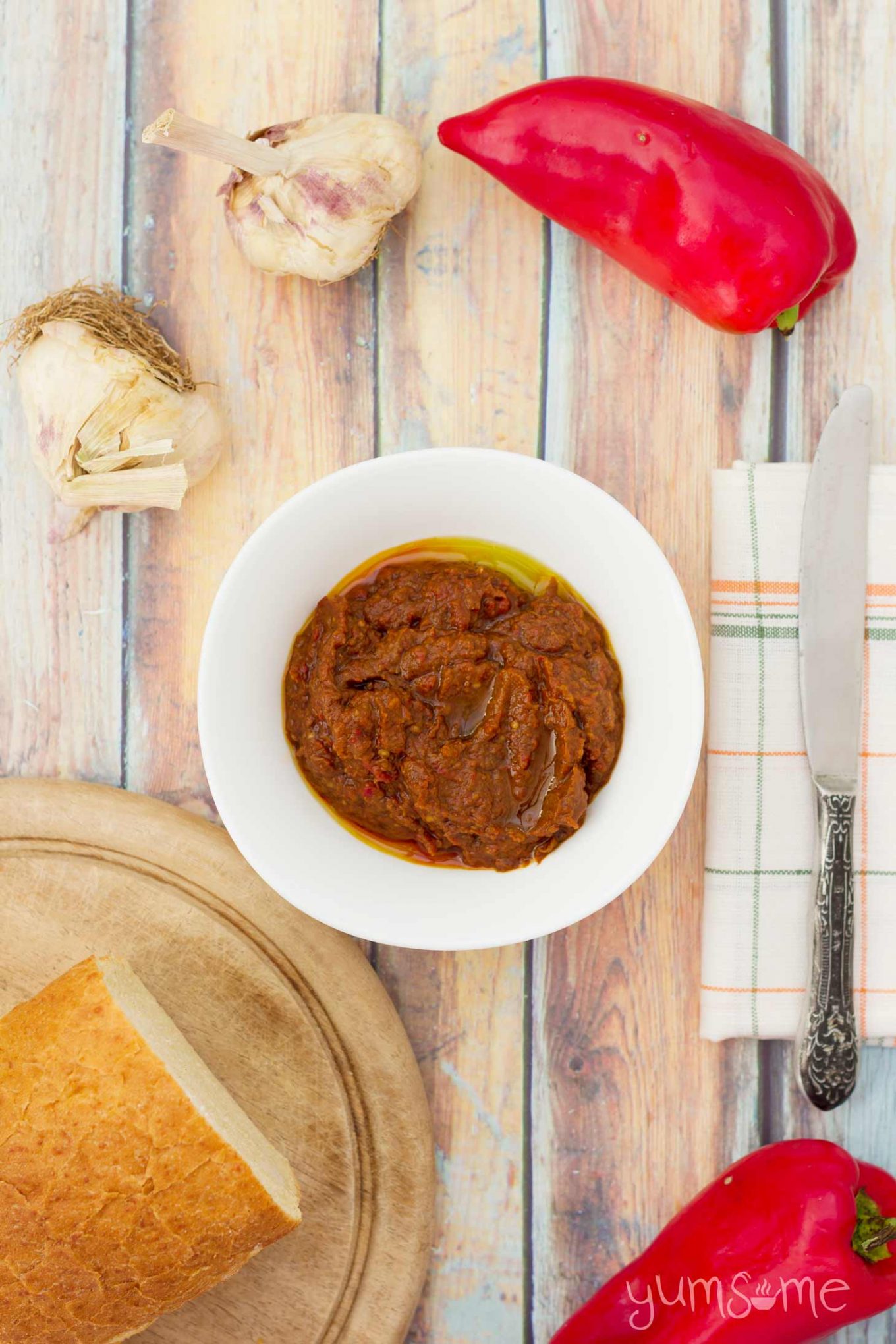 a bowl of ajvar on a table with some bread and red peppers | yumsome.com