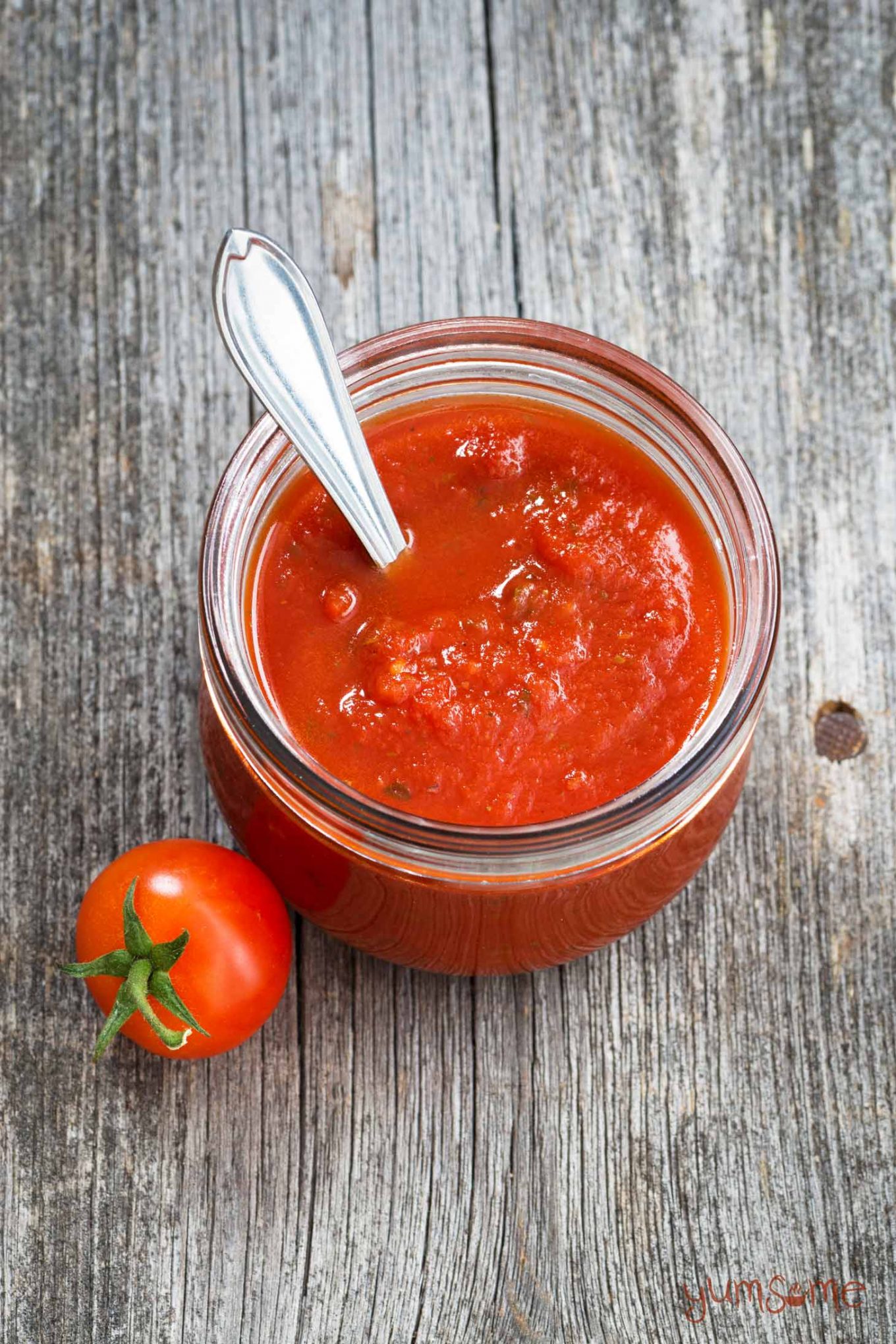 A jar of classic Italian sauce, with a tomato on a grey table.