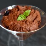 A Martini glass filled with chocolate pudding, topped with two mint leaves.