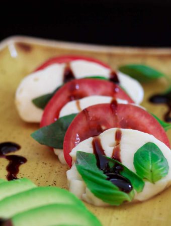 Caprese il tricolore with avocado on a yellow plate.