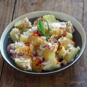 A black and white bowl of vegan potato salad, with paprika and a sprig of tarragon.