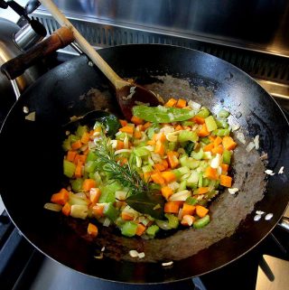 A wok containing chopped vegetables and herbs to make soffritto.