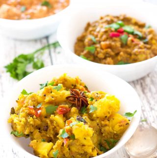 Several white bowls of curry, with aloo masala in the foreground.