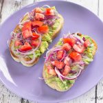 Avocado and tomato bruschetta on a lilac plate.