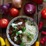 A bowl of chocolate chilli and rice on a wooden table with an assortment of vegetables.