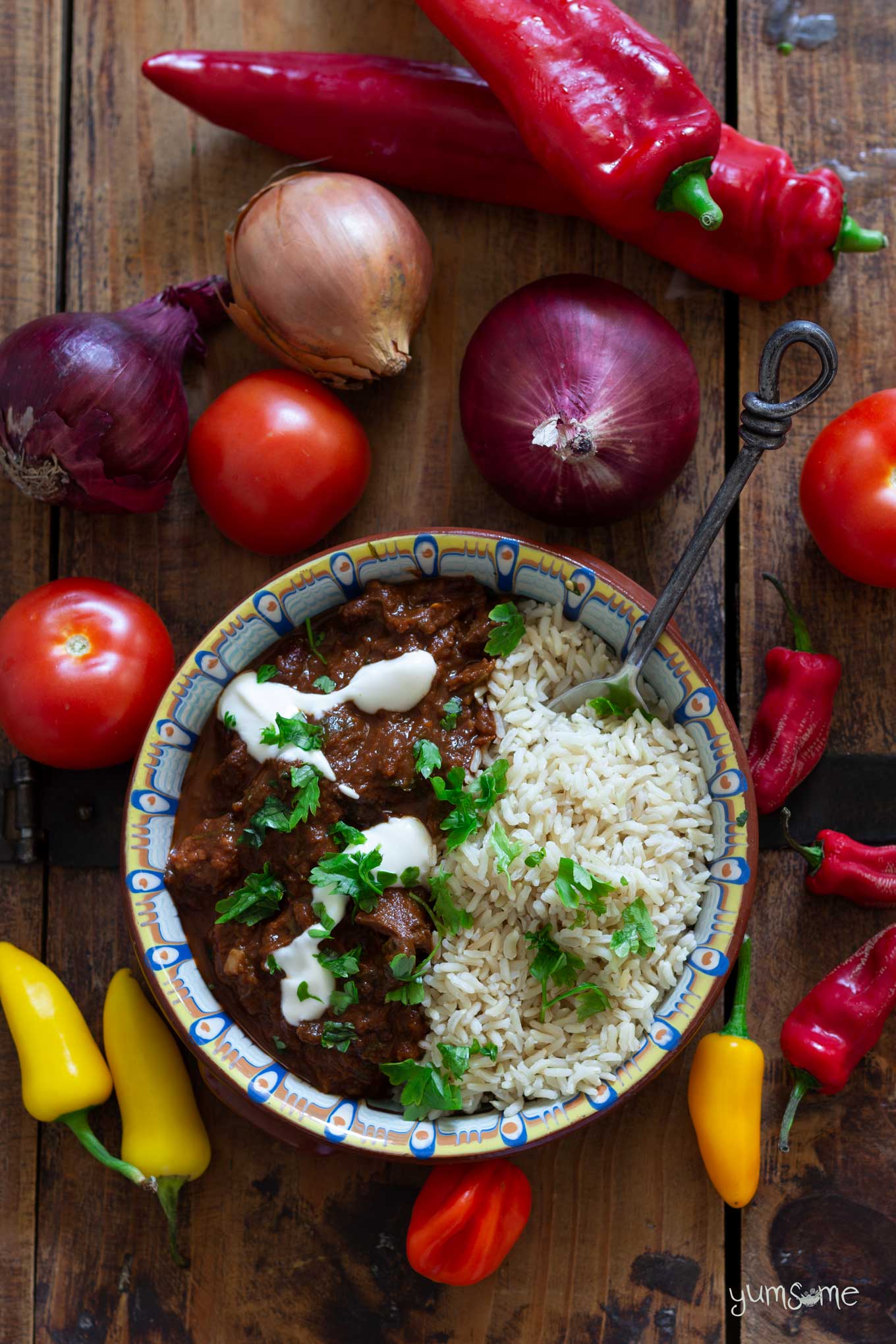 a bowl of chocolate chilli and rice on a wooden table with an assortment of vegetables.