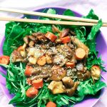 A lilac dish with a bed of vibrant raw spinach leaves, upon which is a stir-fry of mushrooms and vegan sausages.