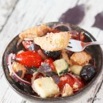 A bowl of vegan panzanella with a fork holding a piece of bread.