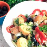 A white bowl containing new potatoes, red peppers, and green herbs.