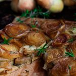 Closeup of caramelized onion tarte tatin on a wooden board, with a slice removed.