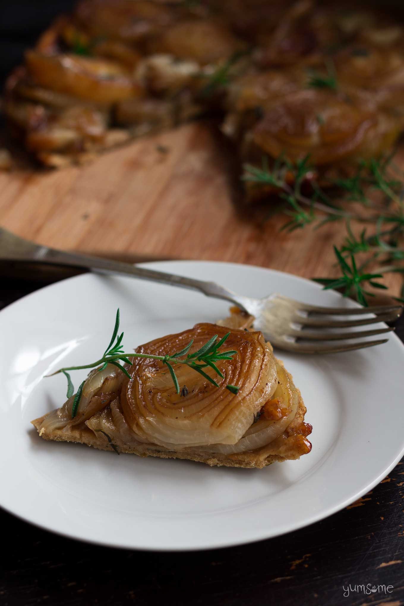 A slice of of caramelized onion tarte tatin on a white plate. with a fork.