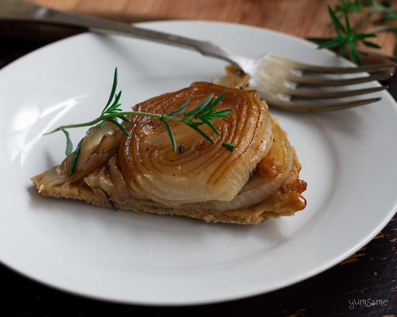 Closeup of a slice of caramelized onion tarte tatin with a fork on a white plate.