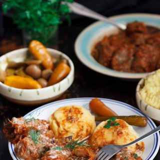 A black table laid with dishes of Romanian sarmale (cabbage rolls), mashed potatoes, and pickled chillies. In the background are more dishes of pickles and sarmale, plus fresh parsley.