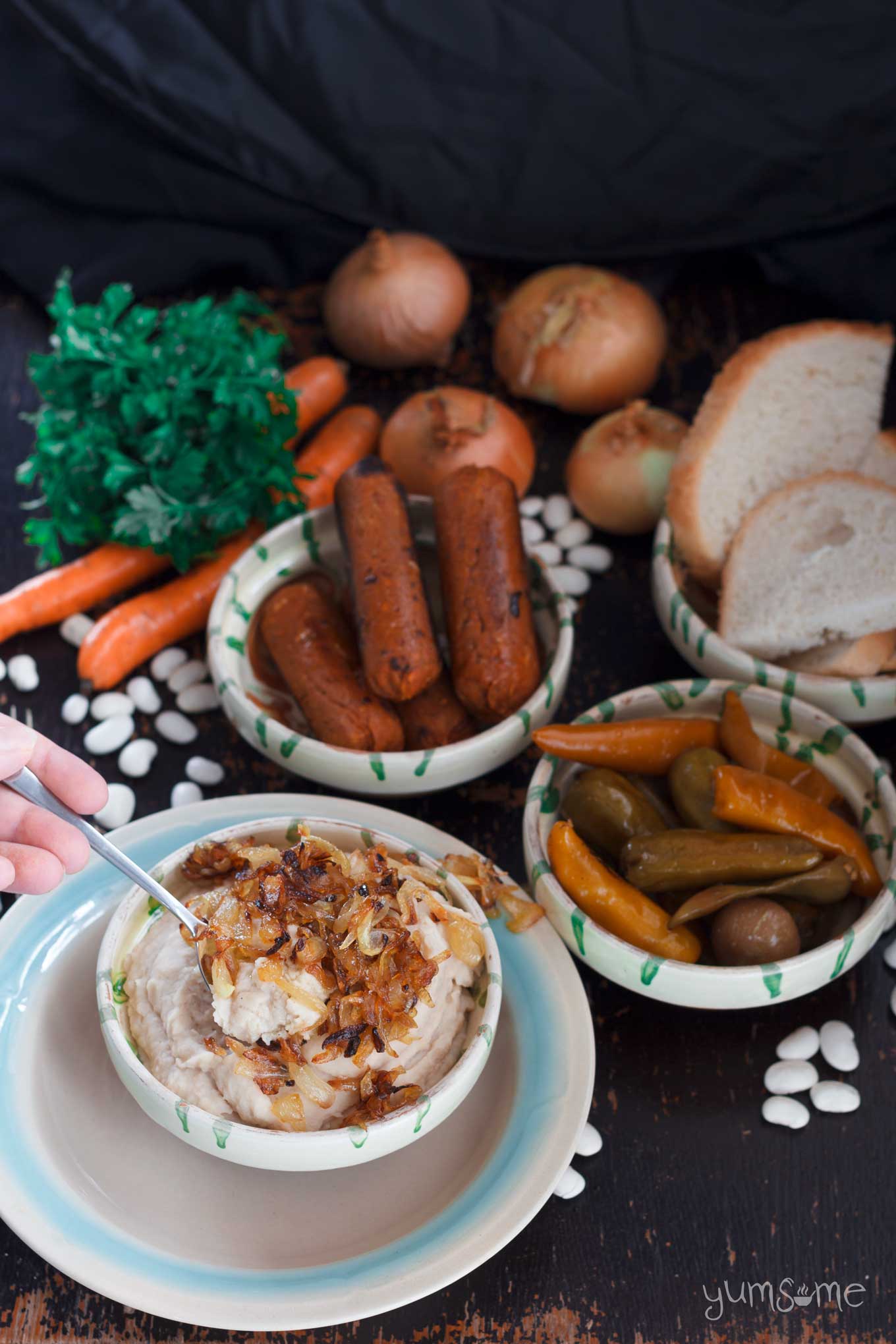 Fasole, sausages, pickles, bread,onions, carrots, white beans, and a large bunch of parsley on a dark table.