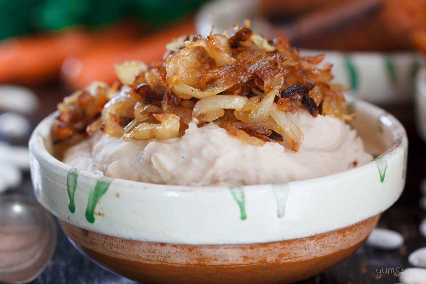 An earthenware bowl of fasole bătută, topped with caramelised onions.