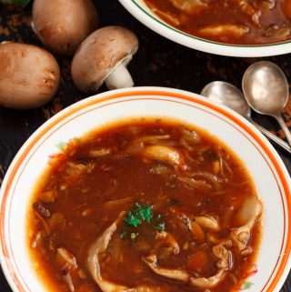 Two dishes of hearty vegan mushroom soup on a black table, with raw chestnut mushrooms and parsley.