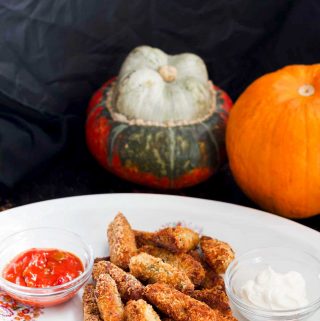 a white plate of vegan baked cheesy pumpkin tots with pumpkins in the background.