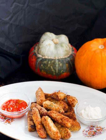 a white plate of vegan baked cheesy pumpkin tots with pumpkins in the background.