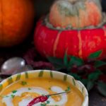 Pumpkins and a bowl of Curried Coconut Butternut Squash Soup against a dark background.