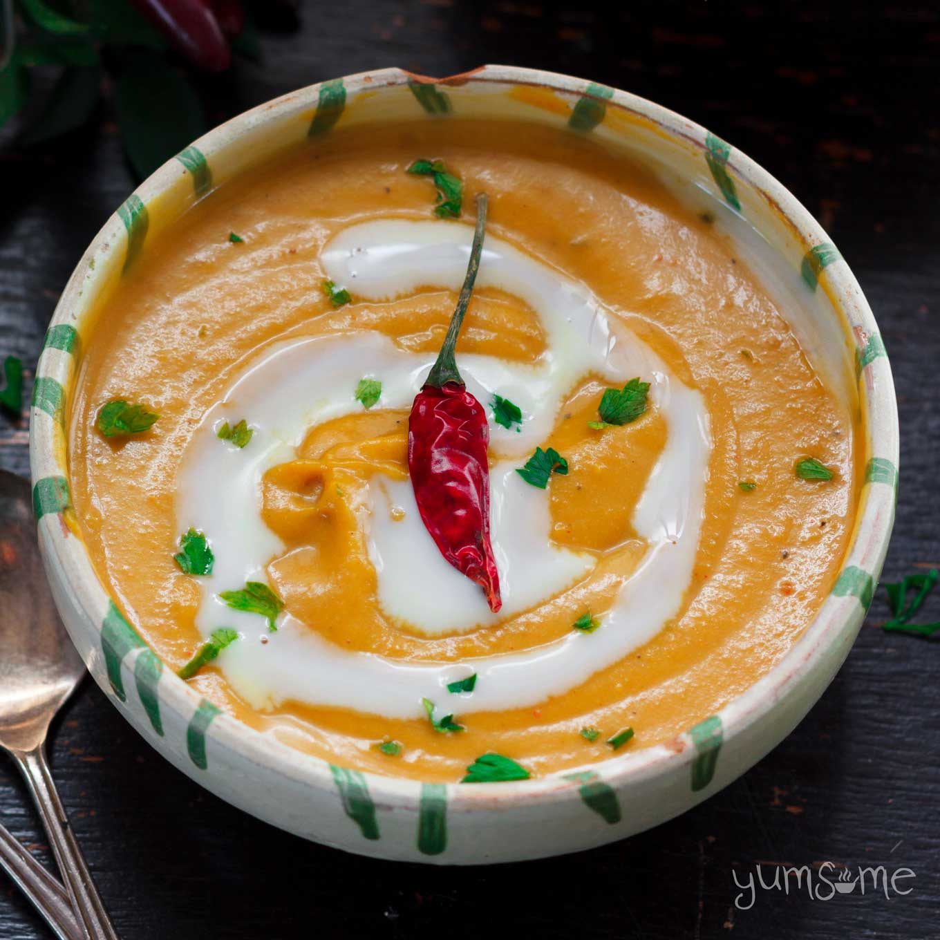 A bowl of Curried Coconut Butternut Squash Soup, with a swirl of cream and a red chilli on top.