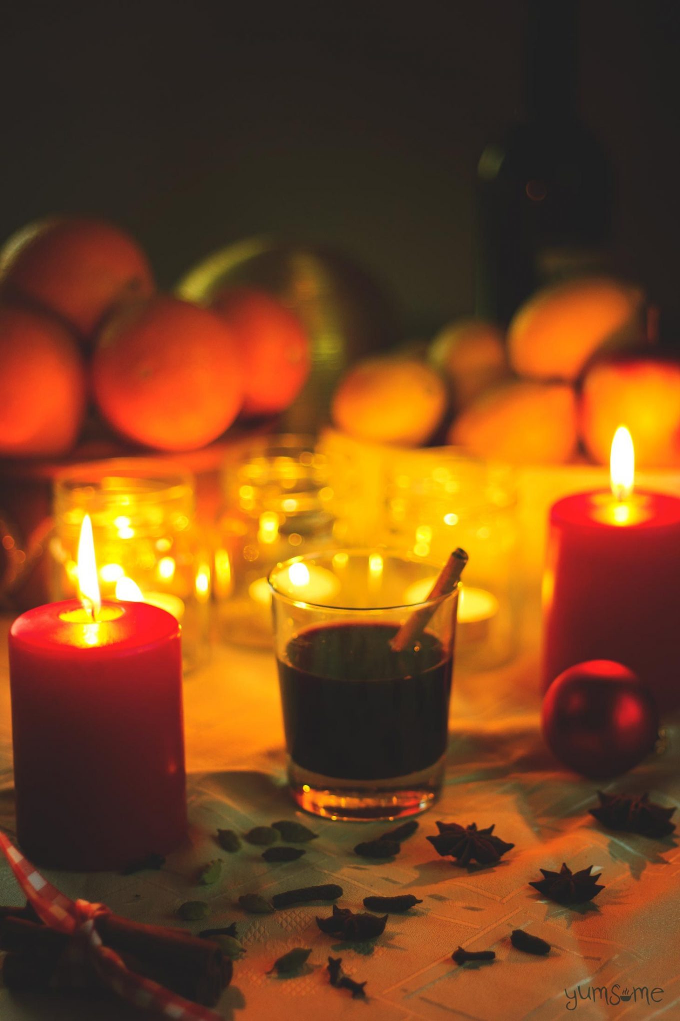 Candlelit glasses of mulled wine, with seasonal fruits in the background.