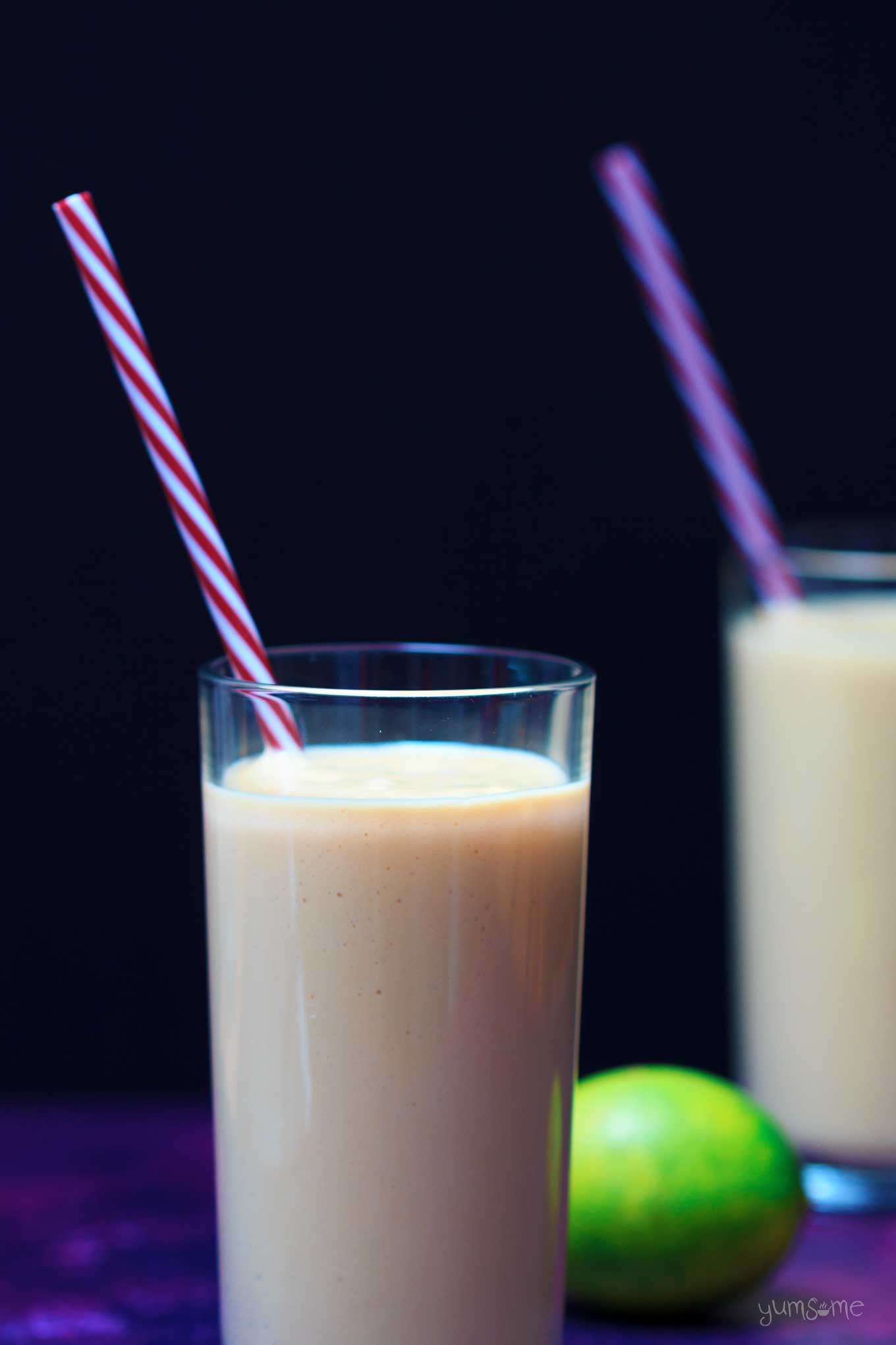 vertical image of two glasses of quick and easy vegan mango and lime lassi with a lime | yumsome.com