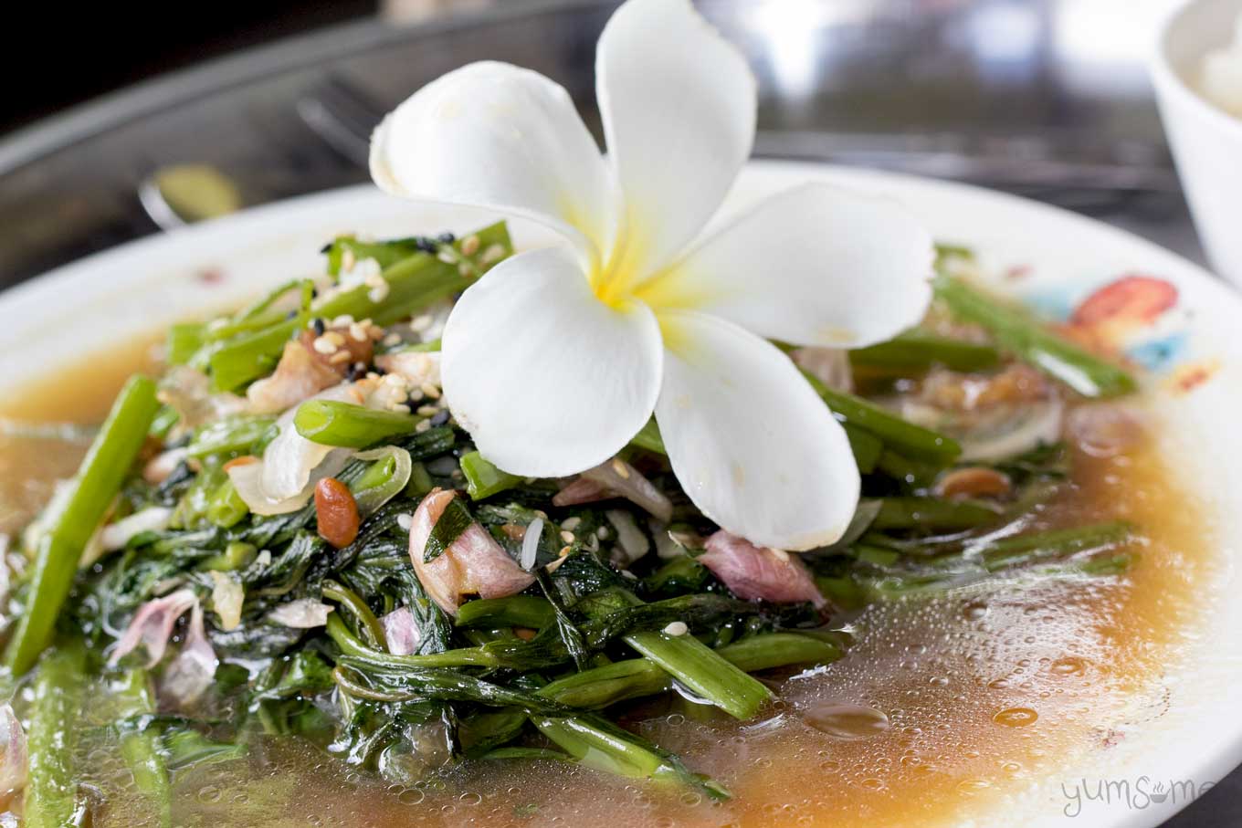 a plate of stir-fried morning glory with a frangipani flower | yumsome.com