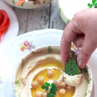 A hand dipping falafel into perfectly smooth and creamy hummus.