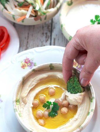 A hand dipping falafel into perfectly smooth and creamy hummus.