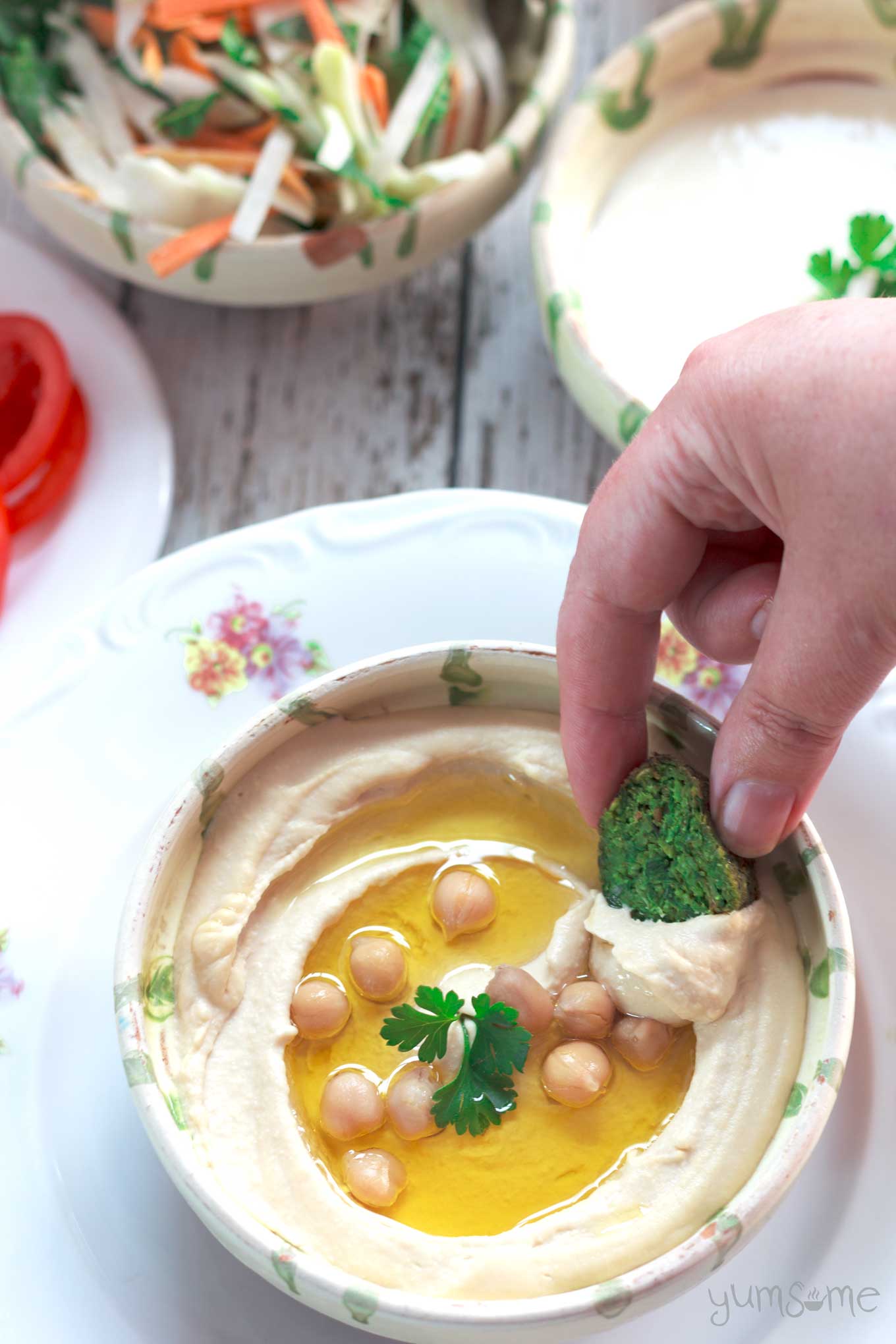 A hand dipping falafel into perfectly smooth and creamy hummus.