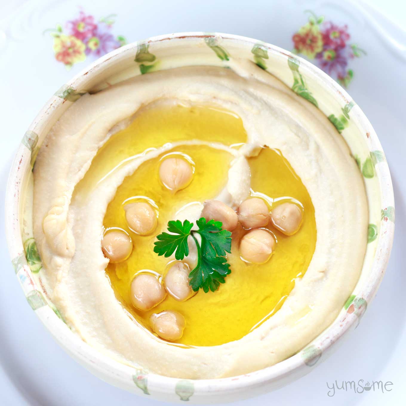 Overhead view of a bowl of hummus with olive oil, chickpeas, and parsley.