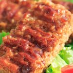 Meaty BBQ seitan ribs on a bed of green leaves.