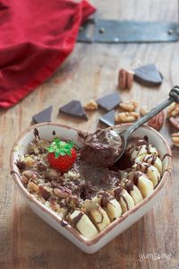 A heart-shaped bowl full of chocolate pudding, bananas, nuts, and salted caramel, with a strawberry on top.