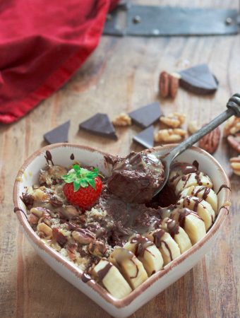 A heart-shaped bowl full of chocolate pudding, bananas, nuts, and salted caramel, with a strawberry on top.