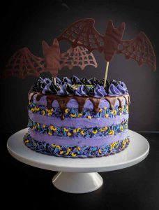 A large purple cake, adorned with chocolate bats and other Halloween candies.