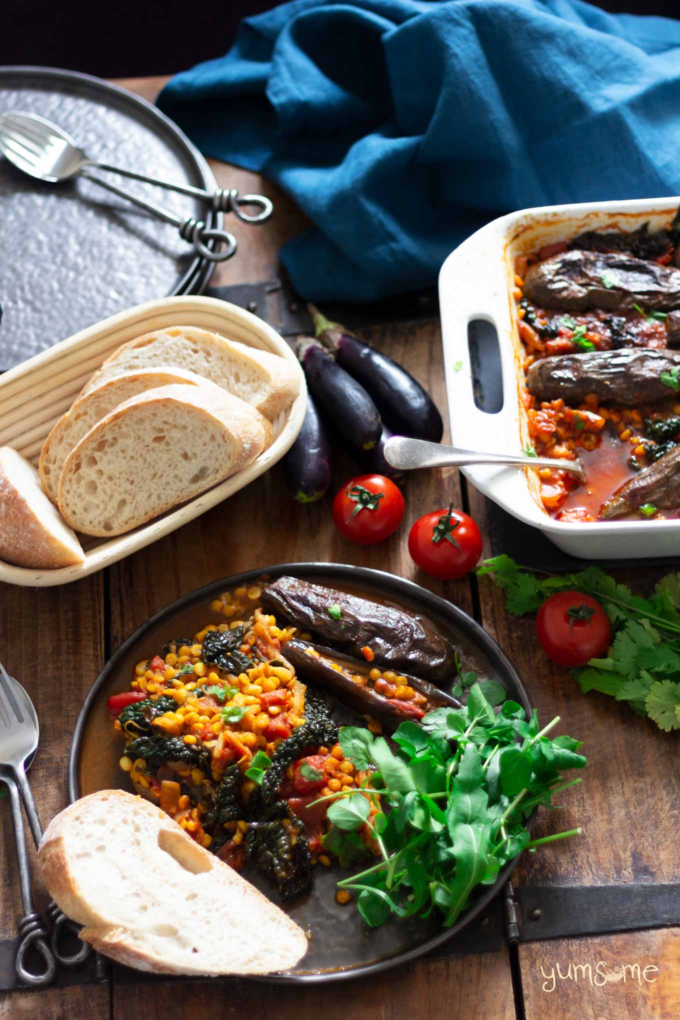 spicy dal, aubergine, and kale casserole on a plate, plus a basket of sourdough bread | yumsome.com