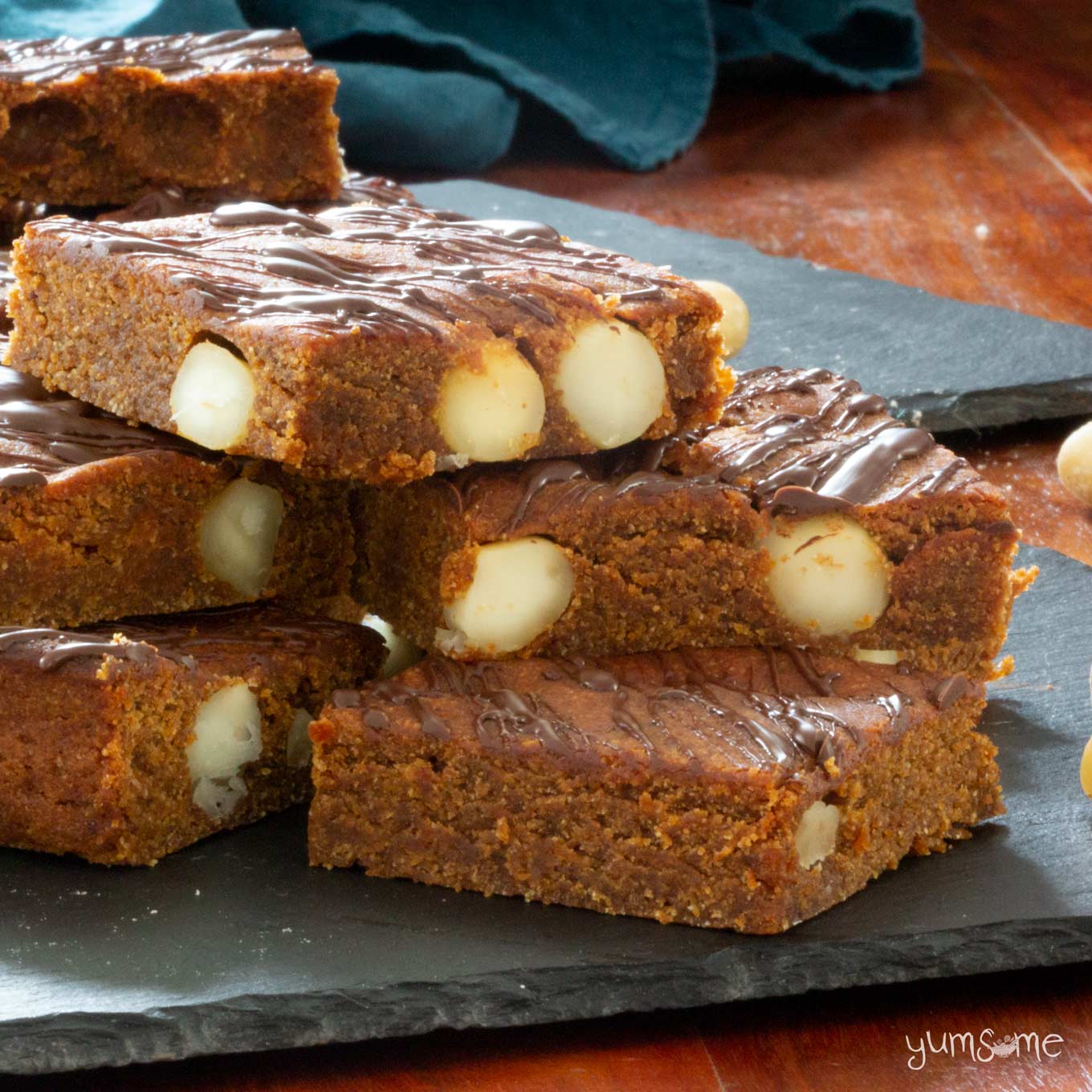 A close up shot of a stack of vegan cookie butter blondies on a slate, showing the macadamias inside.