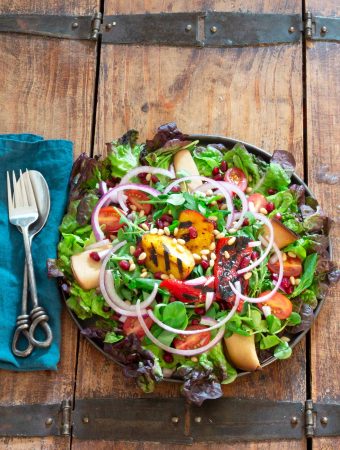 Overhead shot of a bright and colourful plate of grilled nectarine salad on a wooden table with a bright blue napkin, plus flatware.
