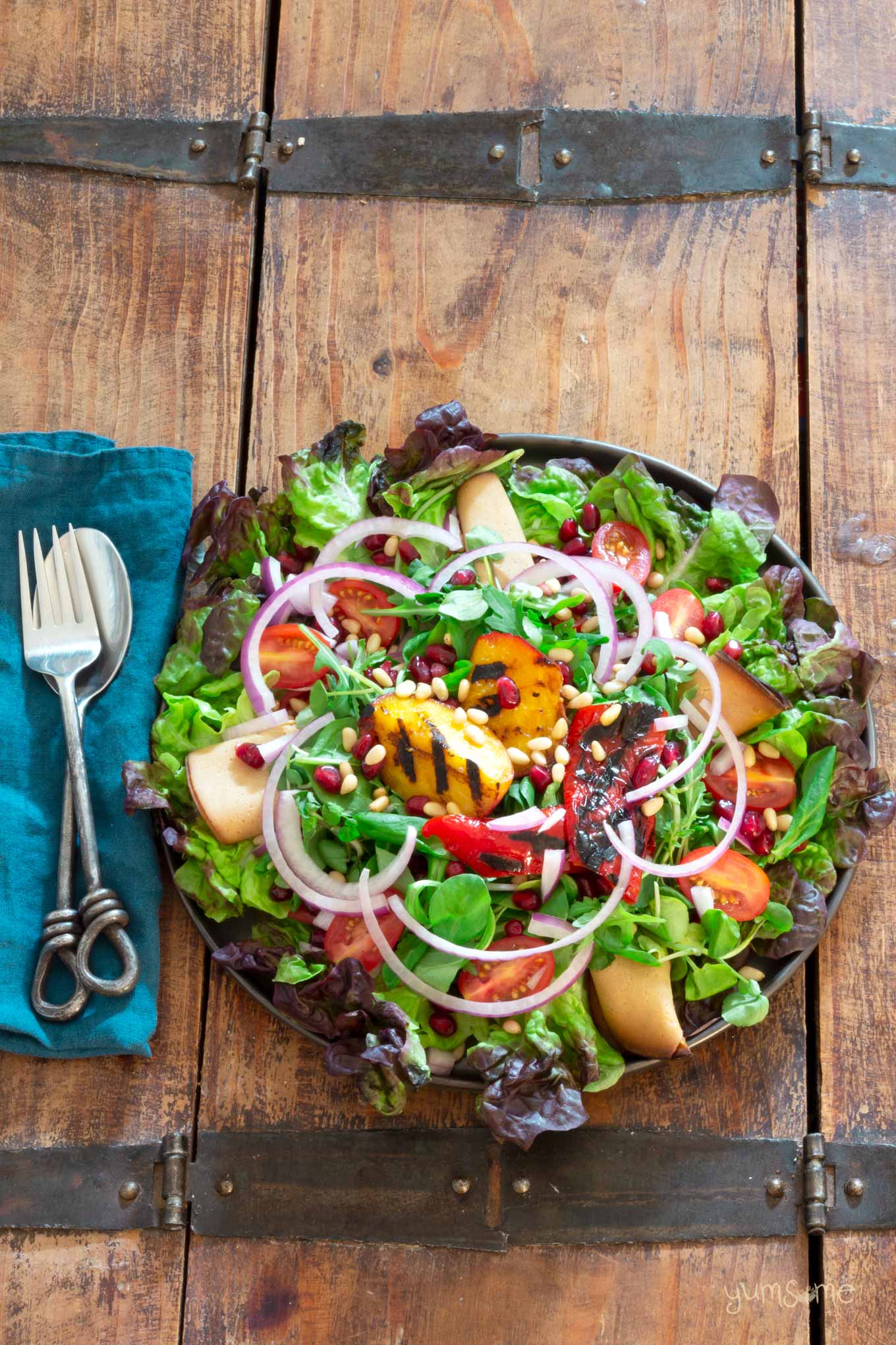 Overhead shot of a bright and colourful plate of grilled nectarine salad on a wooden table with a bright blue napkin, plus flatware.