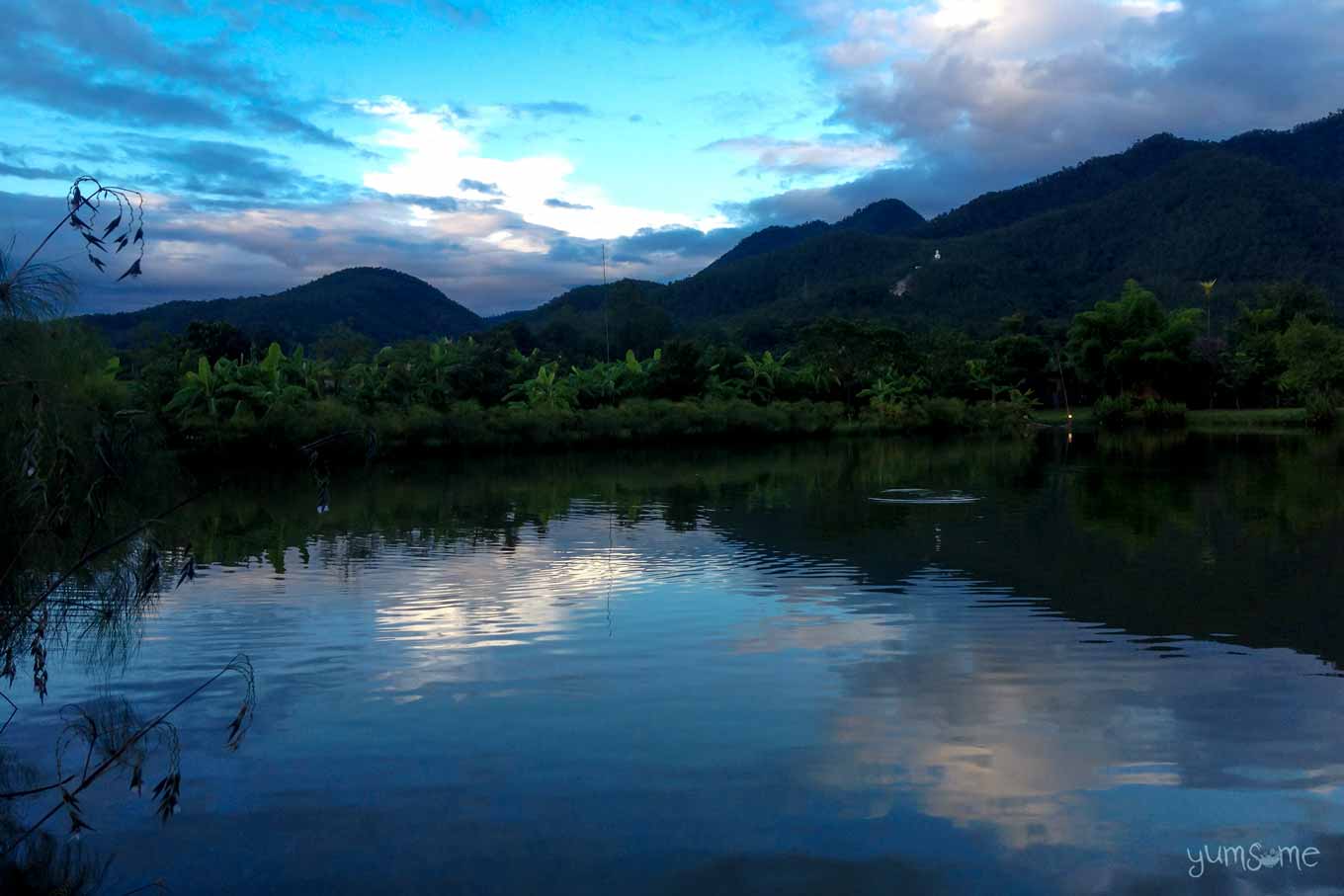 Sunrise over the lake at Bueng Pai Farm, with trees and mountains in the distance.