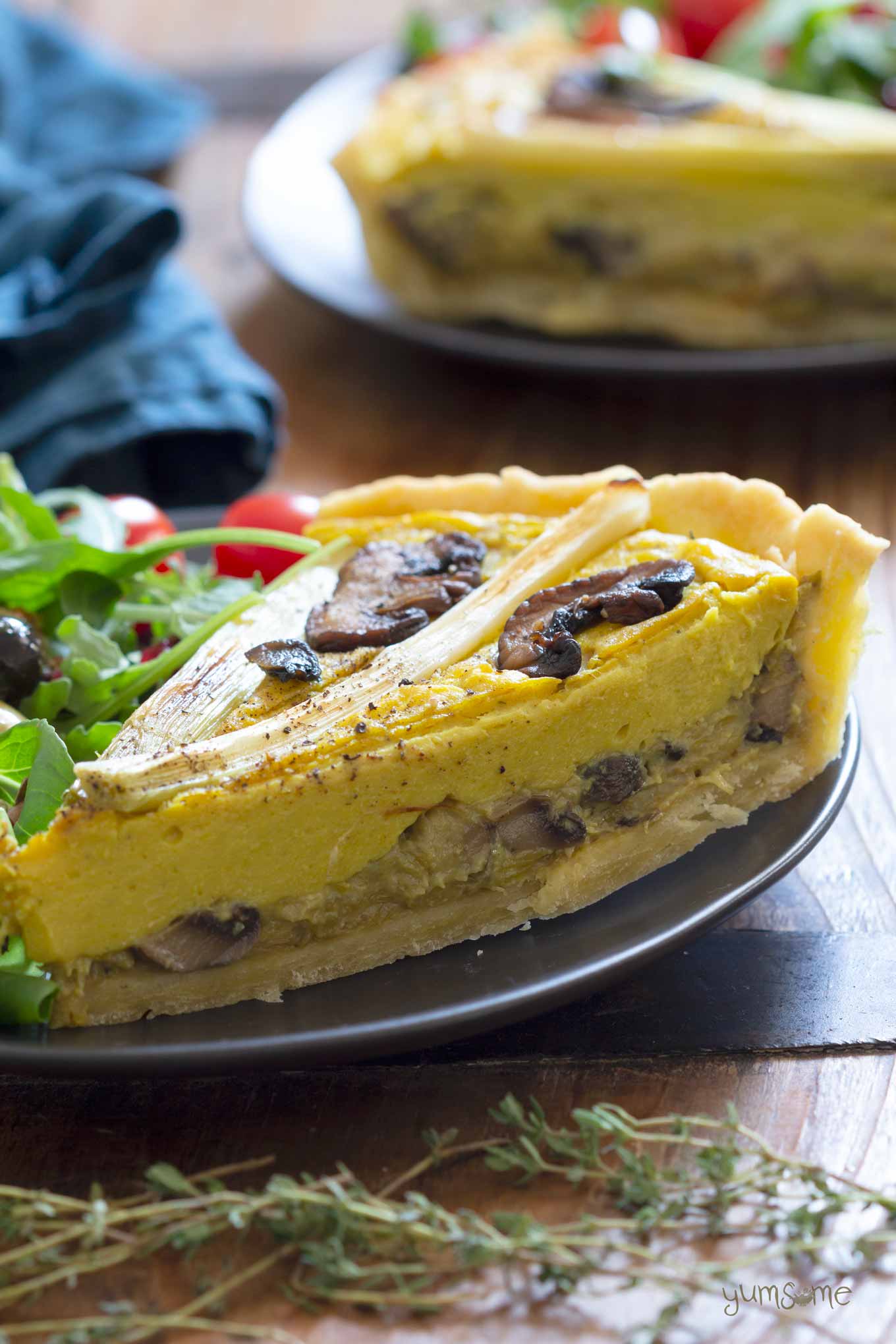 A wedge of mushroom and leek quiche on a black plate.