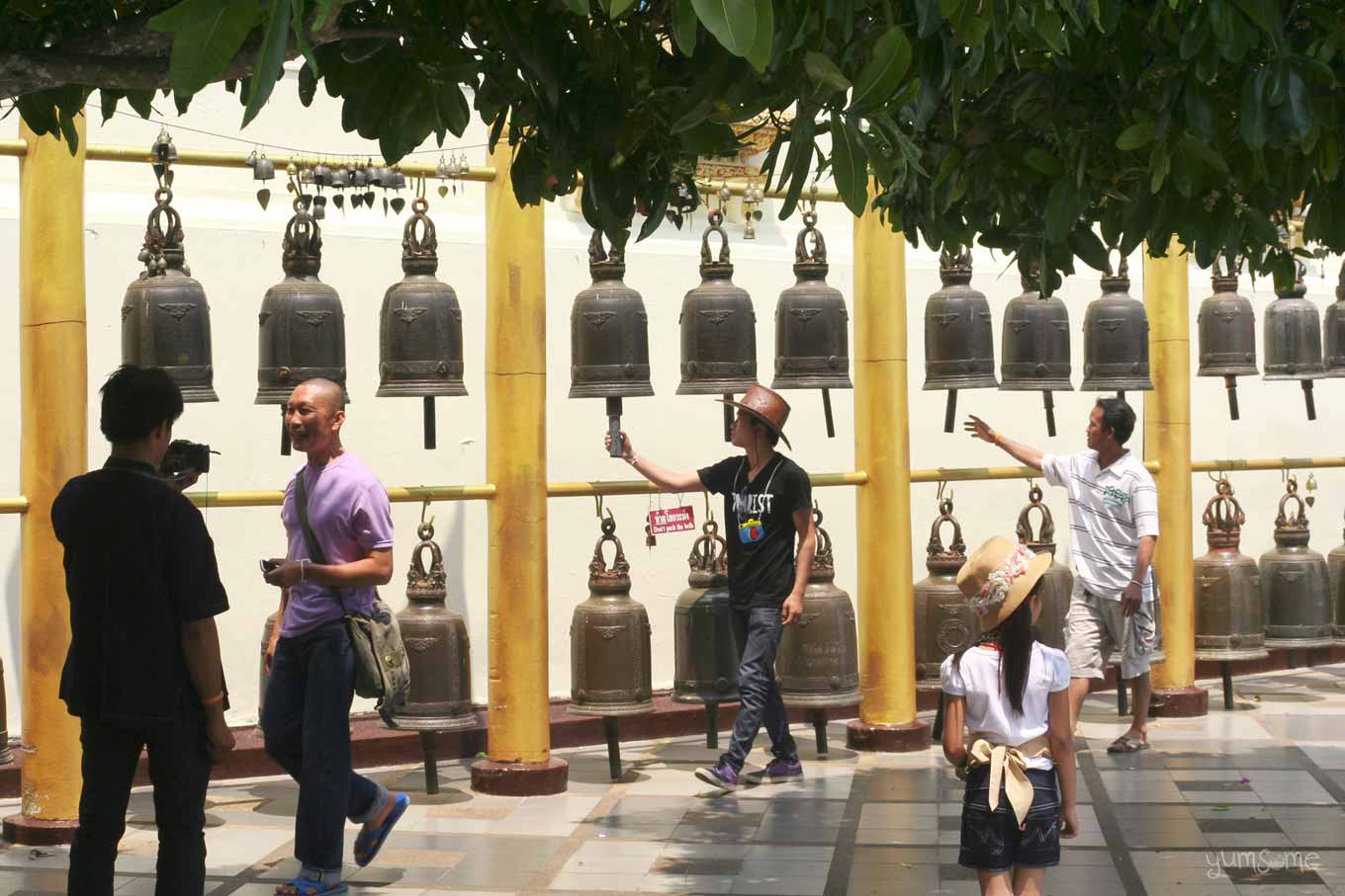 A row of temple bells, with people ringing them, at Wat Doi Suthep.