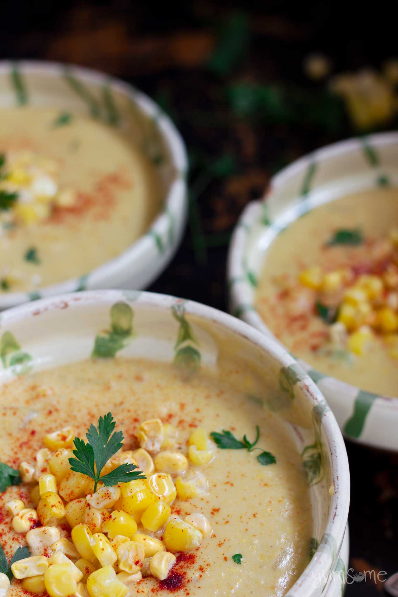 Three bowls of vegan sweetcorn chowder on a black table.