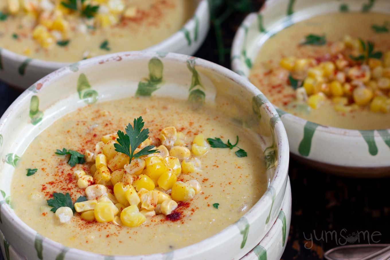 A cream and green bowl containing corn chowder, with extra corn on top.