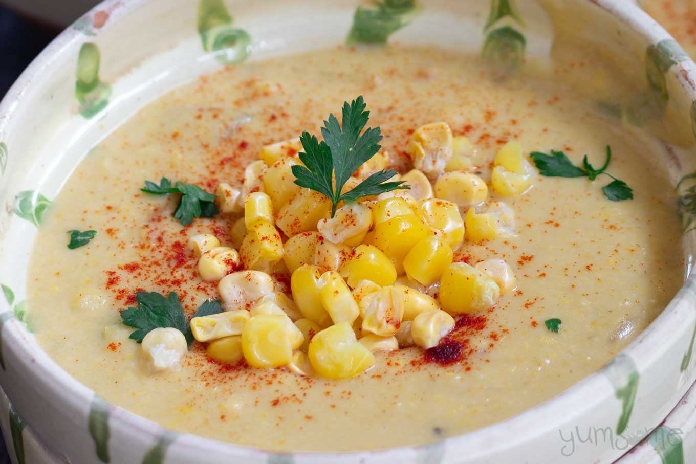 A bowl of vegan sweetcorn chowder with a pile of sweetcorn on top, and garnished with parsley.