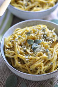 A bowl of spaghetti with sage leaves on top.