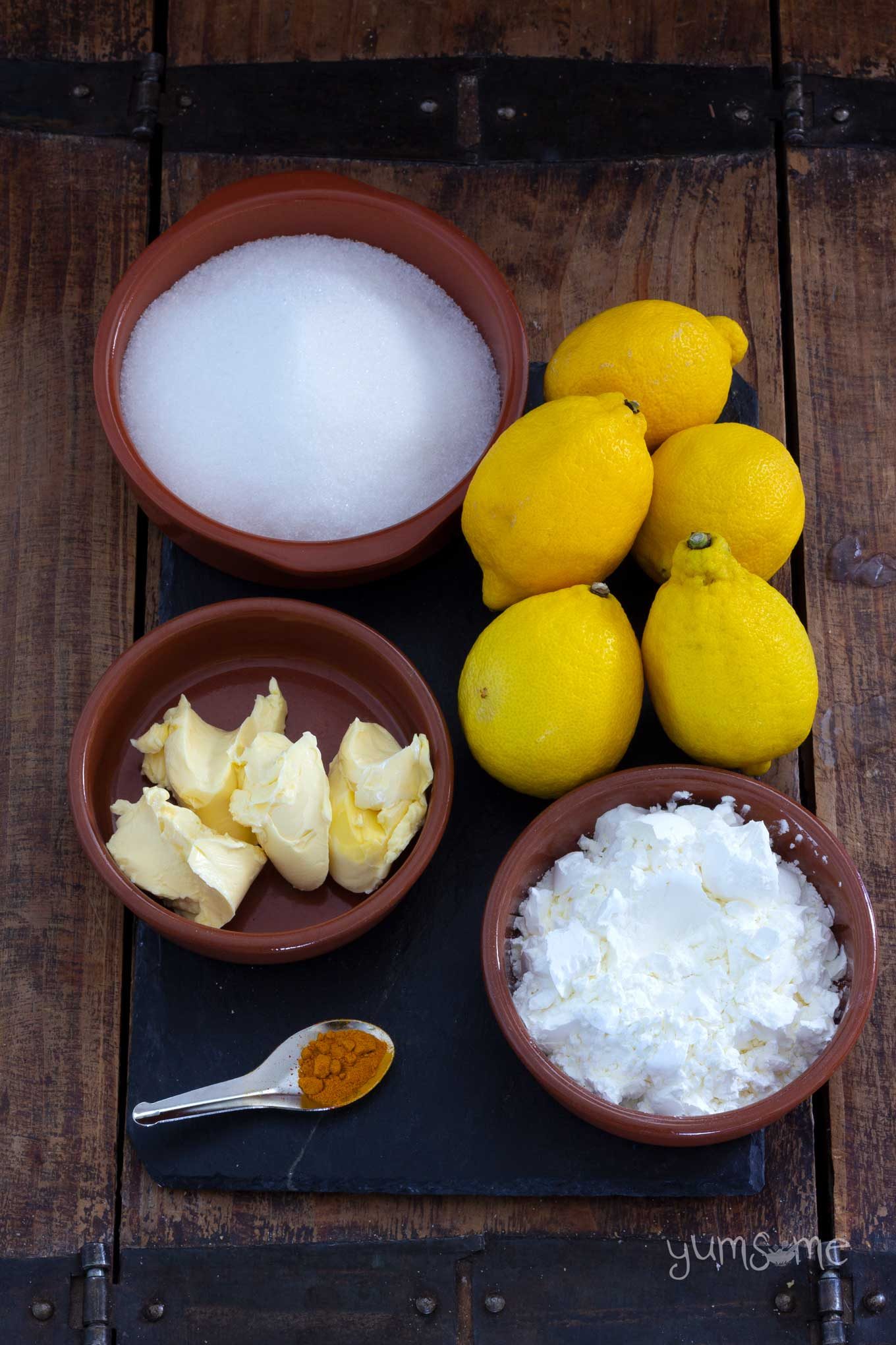 A wooden table with lemons, sugar, cornflour, margarine, and turmeric laid out.