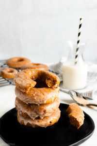 A stack of maple-glazed donuts on a black plate, with a glass of milk in the background.