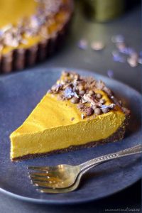 Cacao nibs and chocolate shavings top a slice of yellow pumpkin pie on a black plate.
